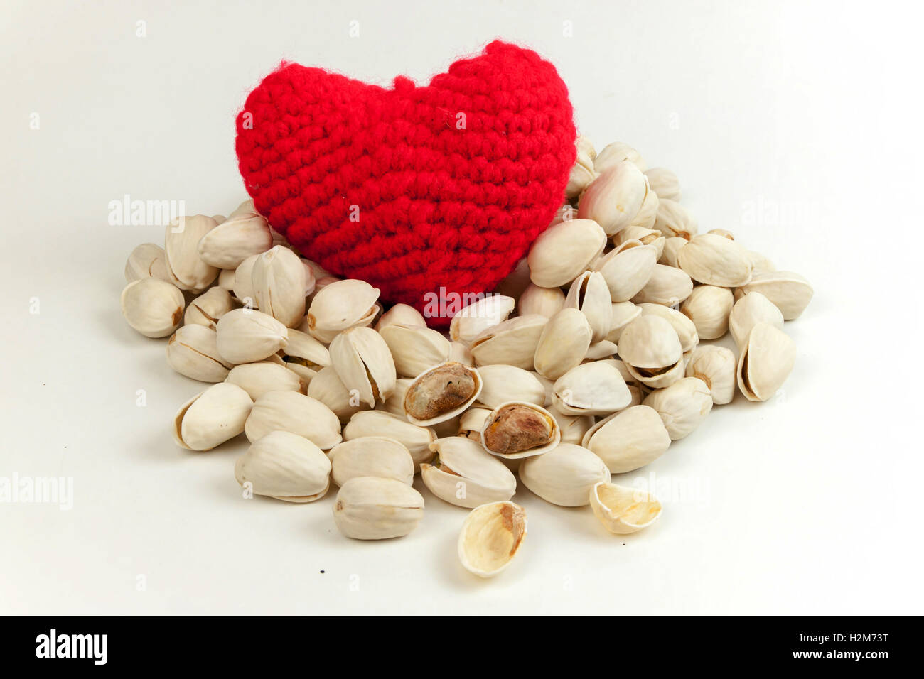 Geröstete Pistazien mit stricken Garn zu einem roten Herz auf weißem Hintergrund, gesundes Essen und Ernährung Stockfoto