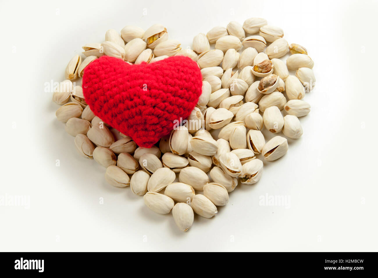 Geröstete Pistazien mit stricken Garn zu einem roten Herz auf weißem Hintergrund, gesundes Essen und Ernährung Stockfoto