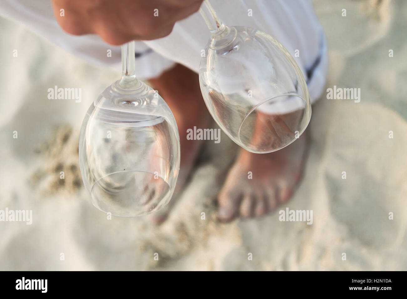 Nahaufnahme von zwei Gläsern in der Hand bei Man barfuß am Strand Stockfoto