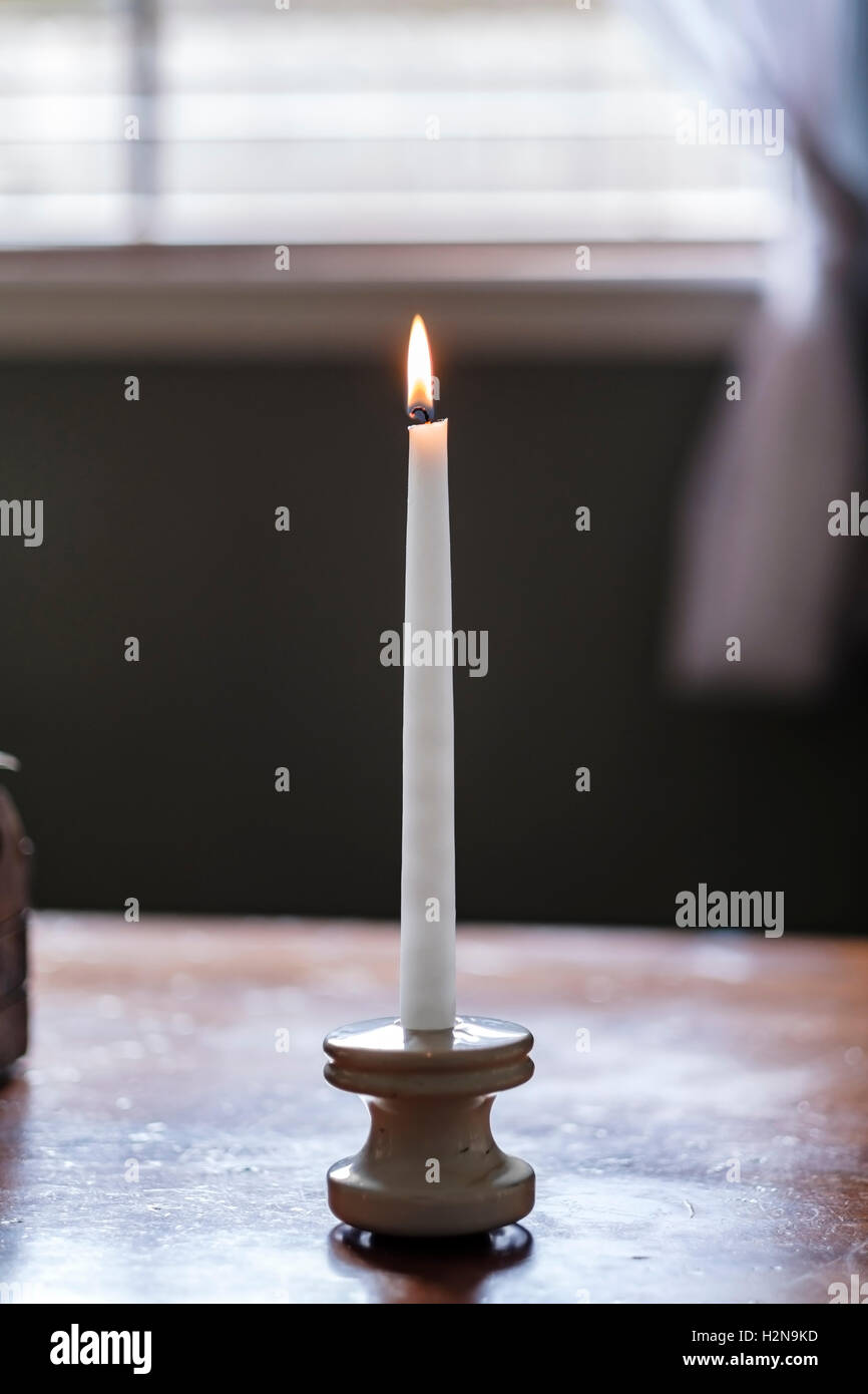 Eine weiße Kerze mit Flamme auf einem Tisch. Stockfoto