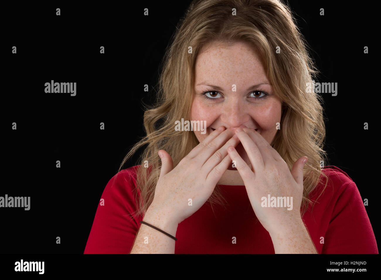 Schüchterne blonde Frau versteckt ihr Lächeln Stockfoto