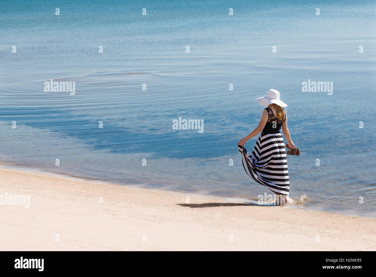 Schöne Frau in einer schwarzen und weißen Sonne-Kleid am Strand entlang spazieren. Stockfoto