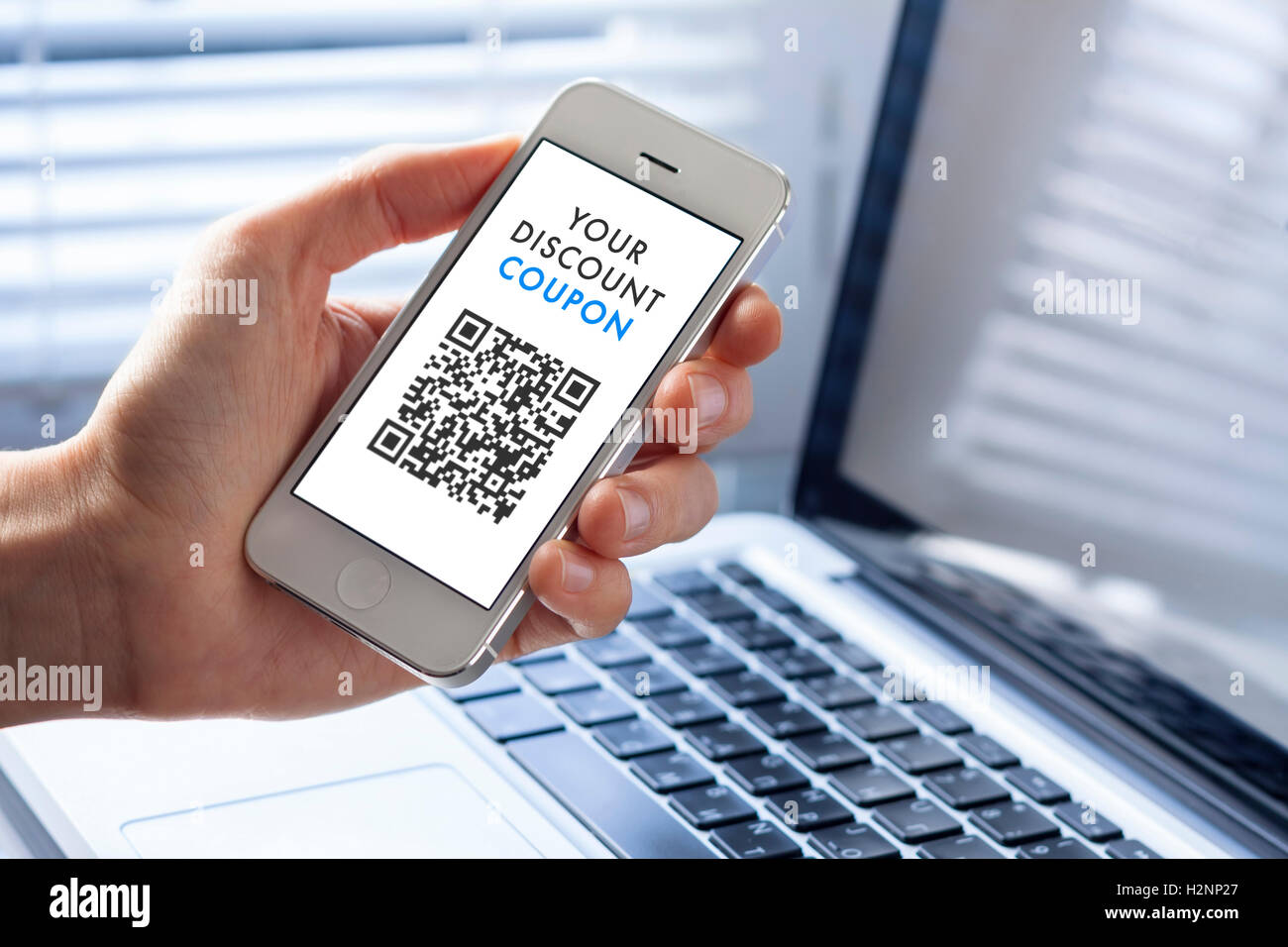 Rabatt-Coupon mit QR-Code auf Smartphone mit Laptop im Hintergrund Stockfoto