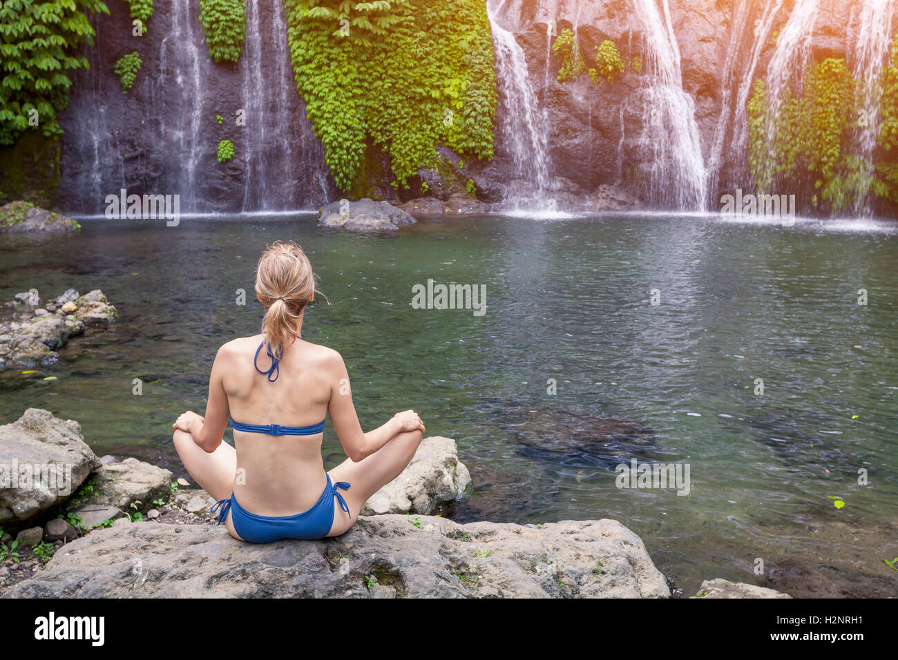 Mädchen üben von Yoga und Meditation im Lotussitz in der Natur in der Nähe eines Wasserfalls Stockfoto
