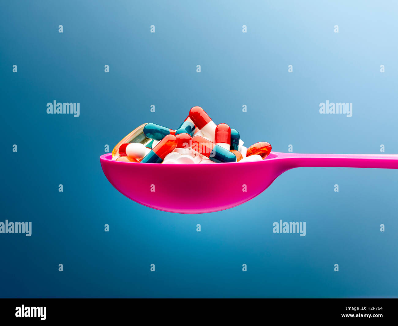 Medizin-Kapseln in rosa Löffel vor blauem Hintergrund Stockfoto