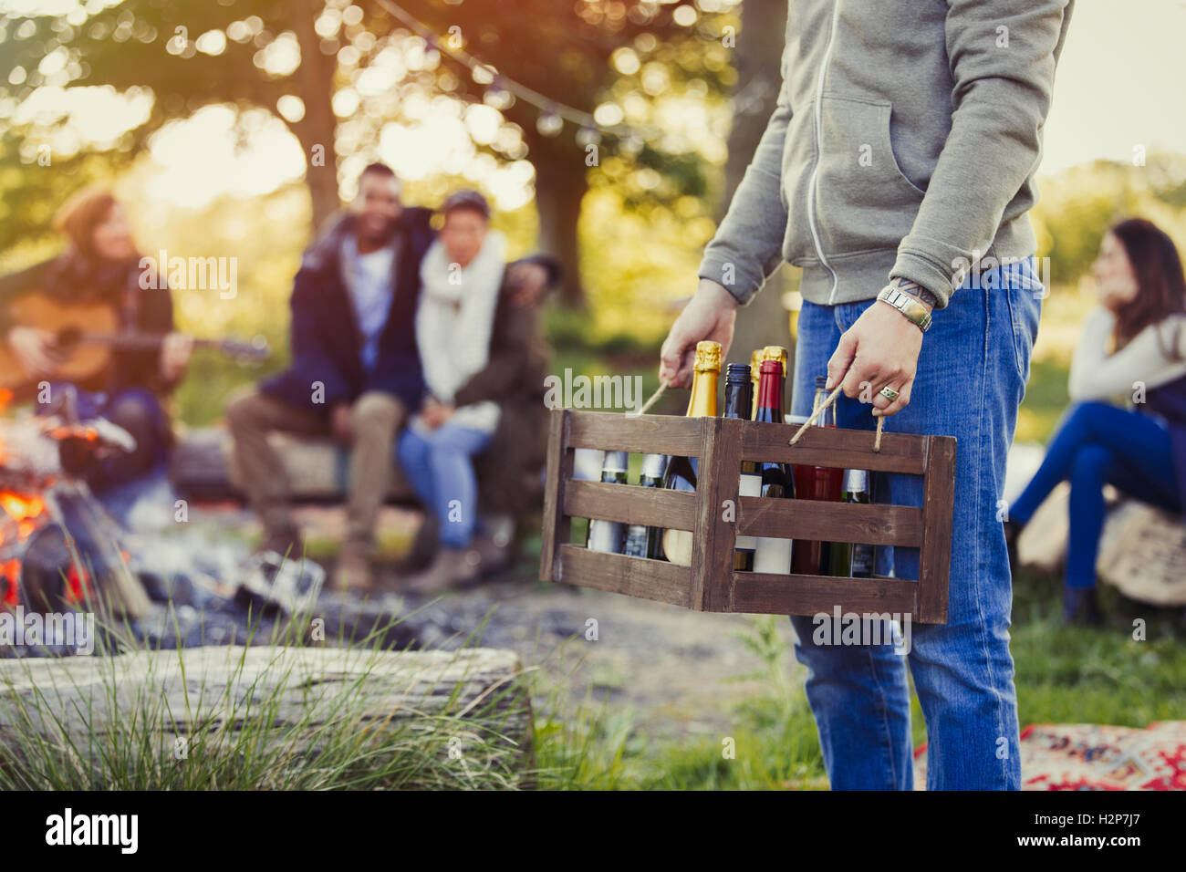Mann trägt Kiste Wein und Bier auf Campingplatz mit Freunden Stockfoto