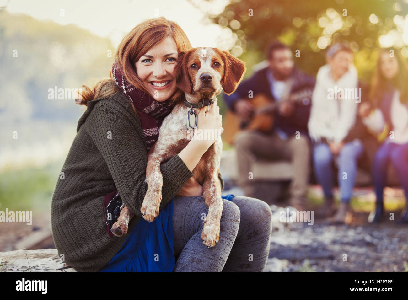 Porträt, lächelnde Frau umarmt Hund auf Campingplatz mit Freunden Stockfoto