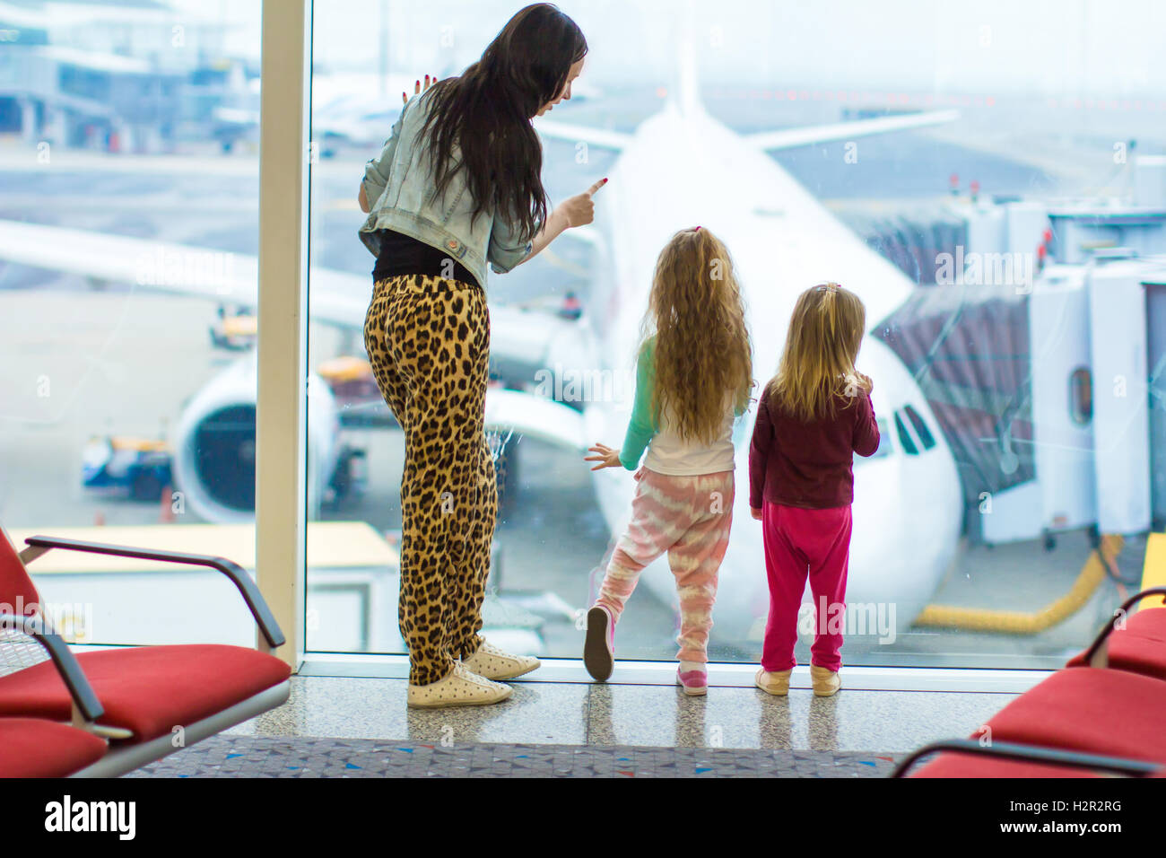 Kleine süße Mädchen und junge Mutter in der Nähe von großen Fenster im Blick auf das Flugzeug Flughafen Stockfoto