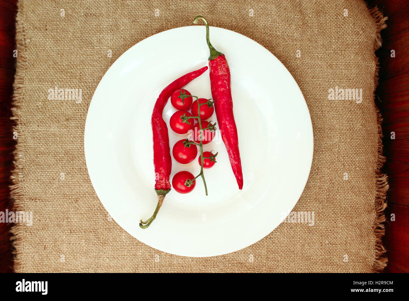 Zweig der rote Kirschtomaten und zwei Pods von Chilischoten auf dem Teller Stockfoto