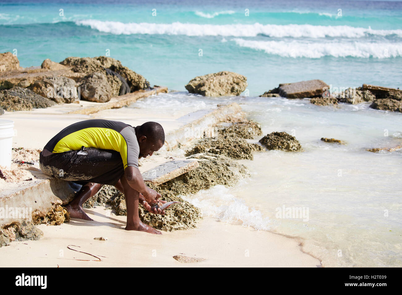 Barbados Hastings Bay Fischer schwarzen männlichen jungen einheimischen Fischen am Strand Meer Armen heruntergekommenen Müll ungepflegt beraubt comm Stockfoto