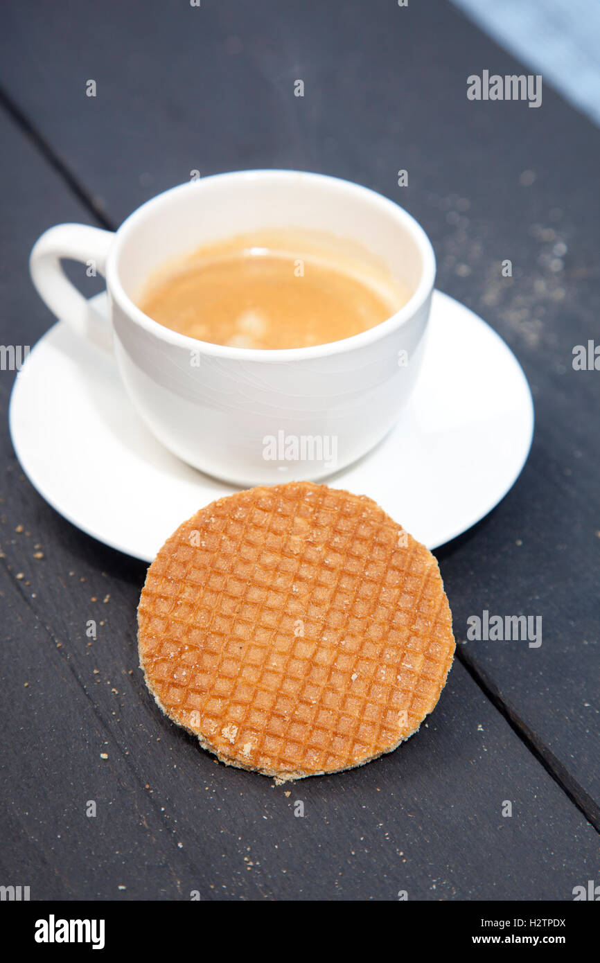 Niederländische Cookie Stroopwafels mit Tasse Kaffee auf schwarzem Hintergrund aus Holz Stockfoto