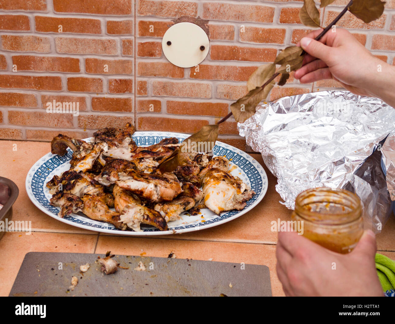 Verglasung BBQ Chicken Stücke. Als letzten Schliff überzieht ein Koch-Assistent Bits des BBQ Chicken mit einer Glasur mit einem grünen Zweig Stockfoto