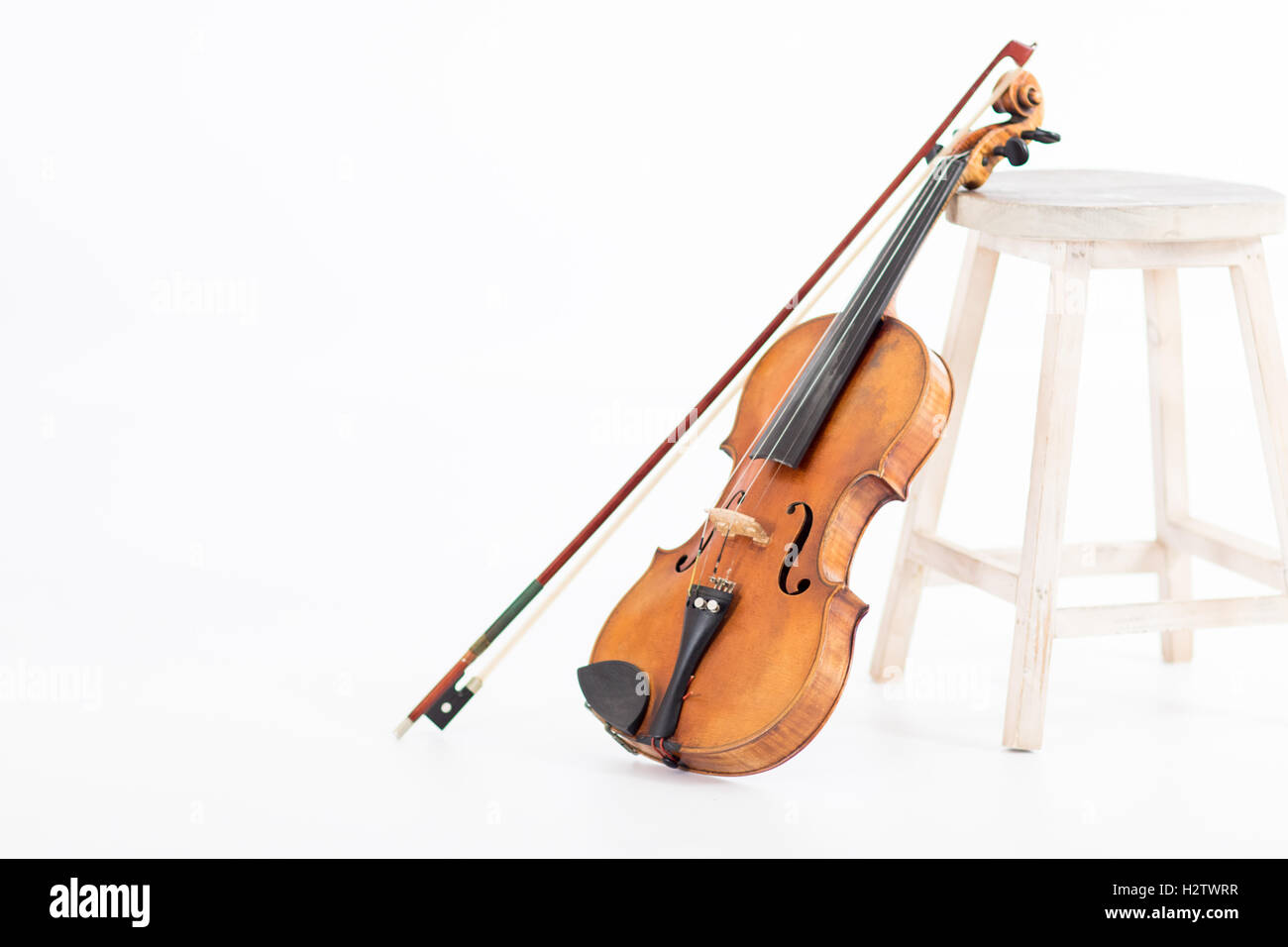 Eine alte Geige stützte sich durch einen Hocker auf weißem Hintergrund Stockfoto