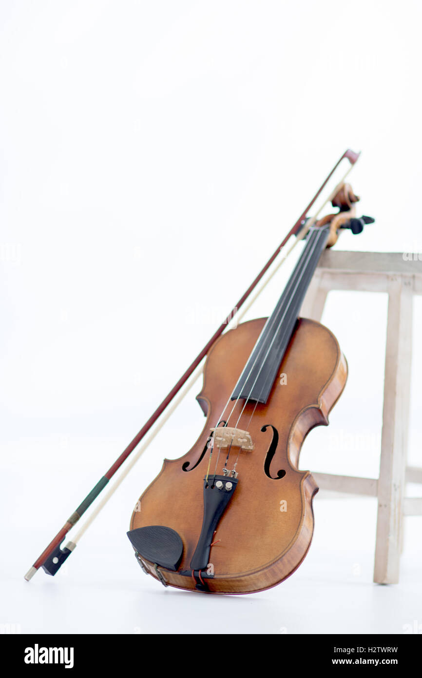 Eine alte Geige stützte sich durch einen Hocker auf weißem Hintergrund Stockfoto