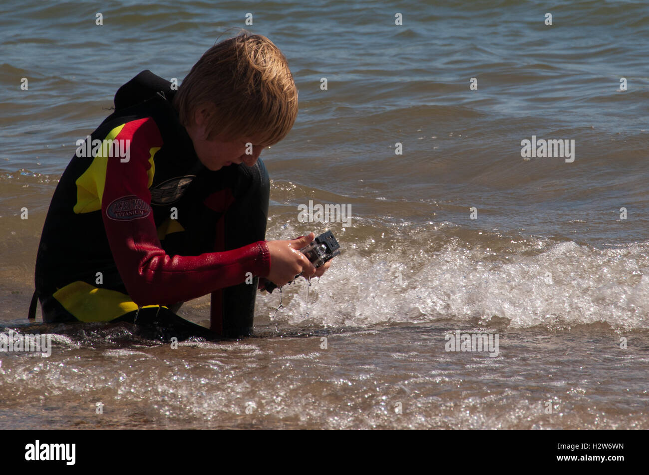 Junge im Neoprenanzug Aufnahmen von Wellen mit kleinen Action-Kamera Stockfoto
