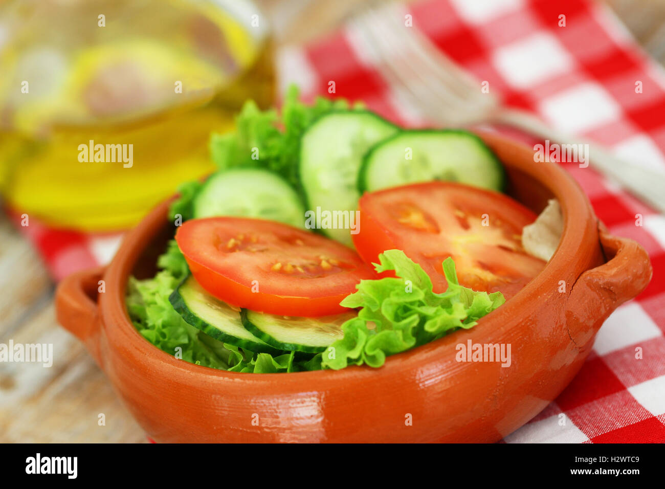 Frischer grüner Salat bestehend aus Salat, Tomaten und Gurken in Ton Schüssel auf kariertem Stoff Stockfoto