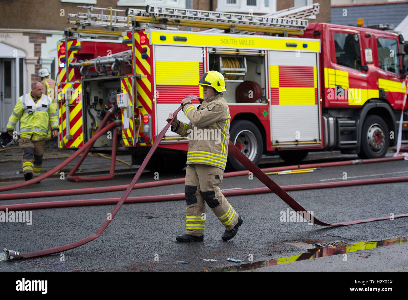 Ein Feuerwehrmann trägt einen Wasserschlauch an die Szene eines Feuers in Birchgrove, Cardiff. Stockfoto
