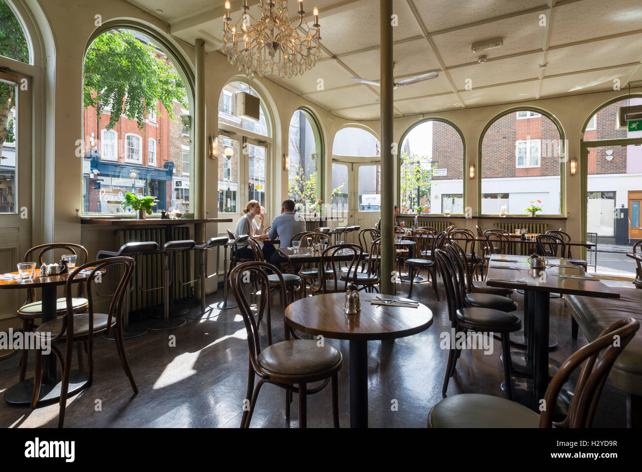 Junges Paar sitzt auf Holzstühlen am runden Tisch zum Frühstück im stilvollen Coco Momo Cafe in Marylebone High Street, Westminster, London, UK Stockfoto