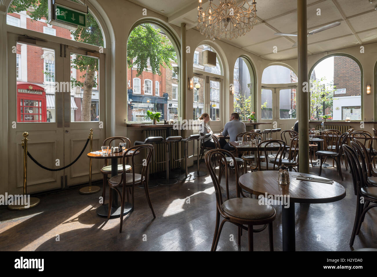 Junges Paar sitzt auf Holzstühlen am runden Tisch zum Frühstück im stilvollen Coco Momo Cafe in Marylebone High Street, Westminster, London, UK Stockfoto