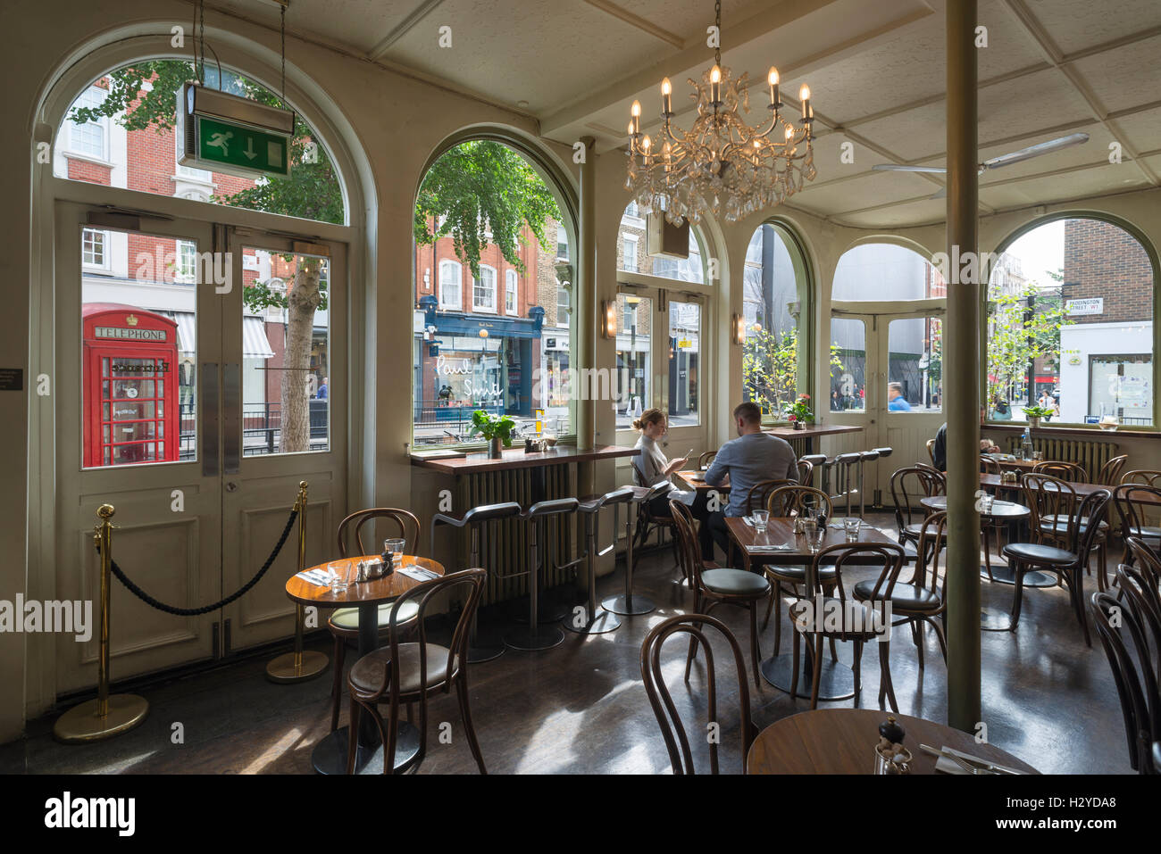 Junges Paar sitzt auf Holzstühlen am runden Tisch zum Frühstück im stilvollen Coco Momo Cafe in Marylebone High Street, Westminster, London, UK Stockfoto