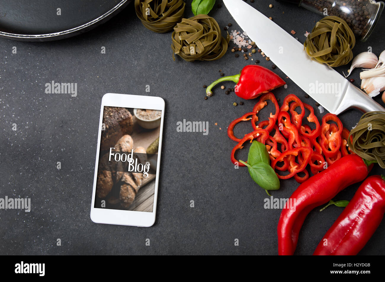 Smartphone mit Foodblog Anwendung auf Stein Arbeitsplatte liegend und umgeben von frischer Kräuter und Gewürze Stockfoto