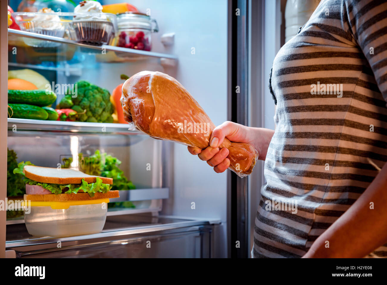 Hungrig, dicke Frau, eine große Putenschenkeln in den Händen hält und neben dem offenen Kühlschrank steht. Ungesunde Lebensmittel. Stockfoto