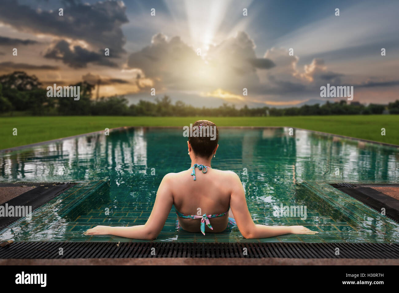 Urlaub Lifestyle Szene der junge Frau sitzt im Pool am Morgen rechtzeitig mit Sonnenuntergang Landschaftsansicht in unscharfen Hintergrund Stockfoto
