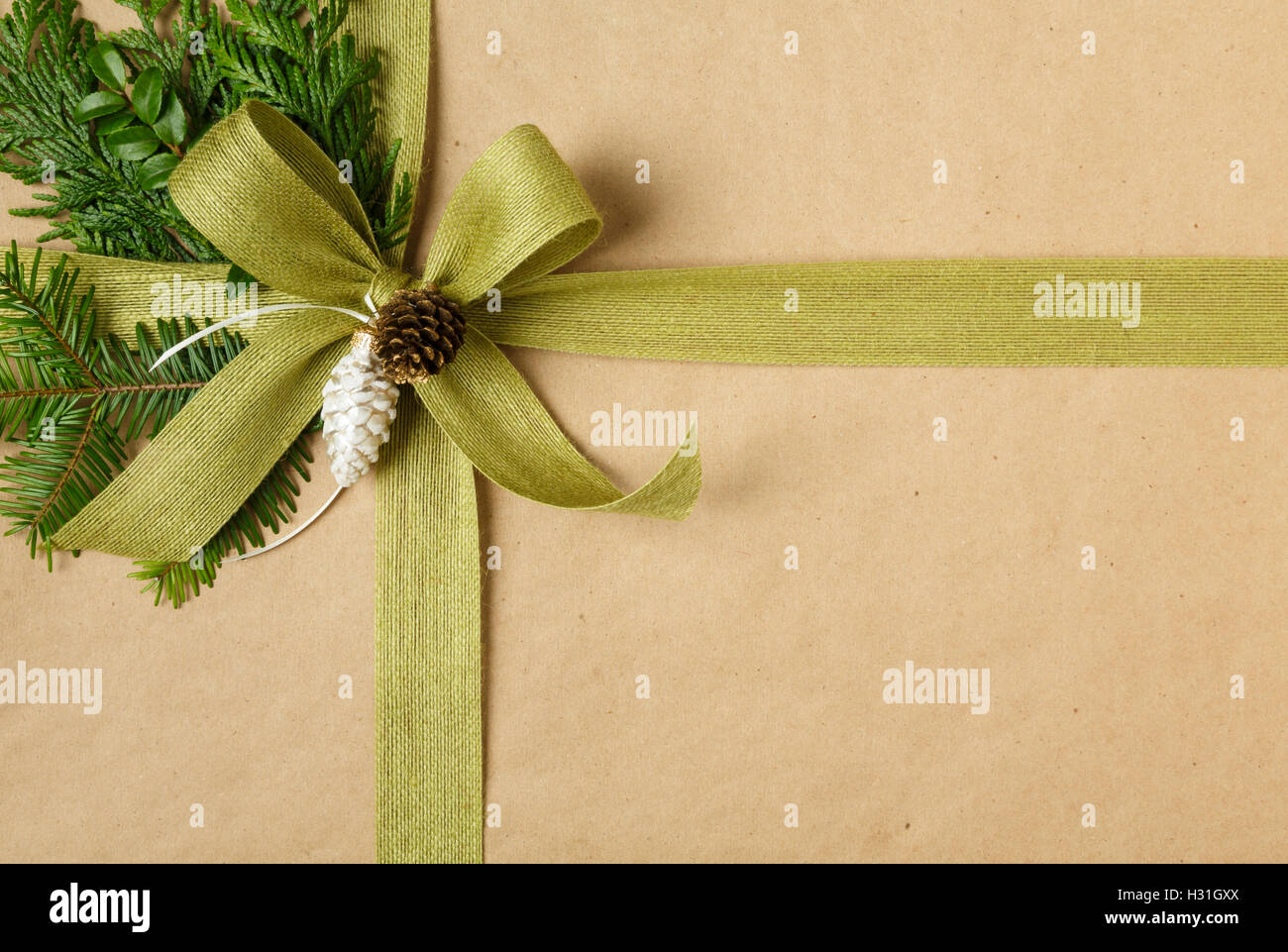 Nahaufnahme von Bogen und natürliche Dekorationen auf Weihnachtsgeschenk. Weihnachtsgeschenk in Recycling-Geschenkpapier eingewickelt. Stockfoto