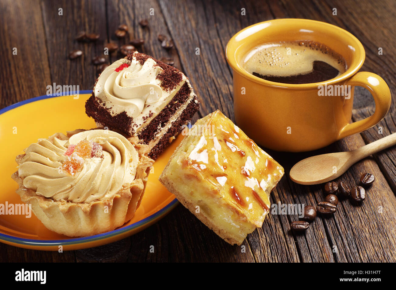 Drei Kuchen in gelbes Schild und Kaffeetasse auf alten Holztisch Stockfoto