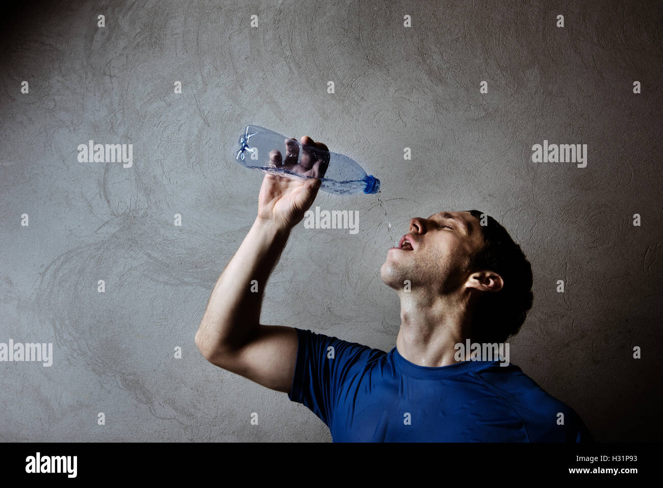 Muskel-Mann trinkt Wasser aus Plastikflasche auf graue Wand Hintergrund Stockfoto