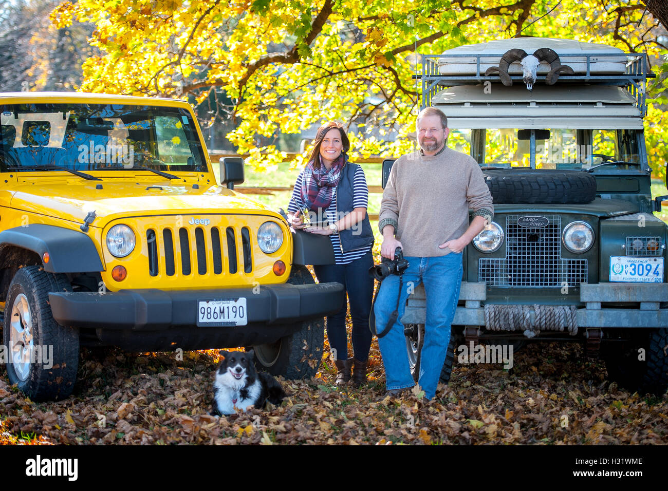 Ein Mann und Frau stand vor einem Jeep Wrangler und Land Rover mit einem Border Collie. Stockfoto