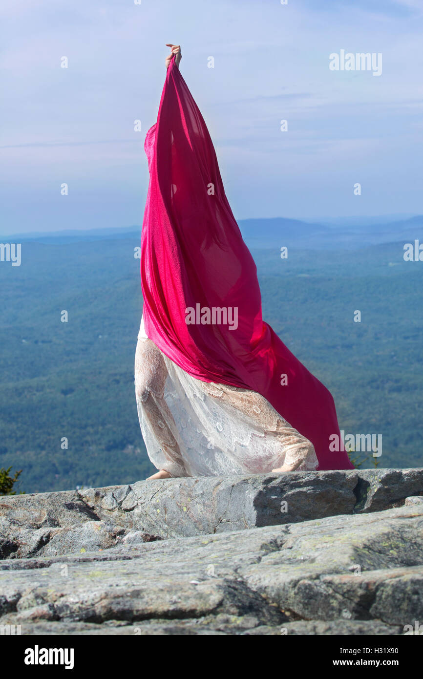 Tänzerin in weißes Kleid gehüllt in rotem Stoff im Wind am Gipfel des Mt. Kearsarge, NH. Stockfoto