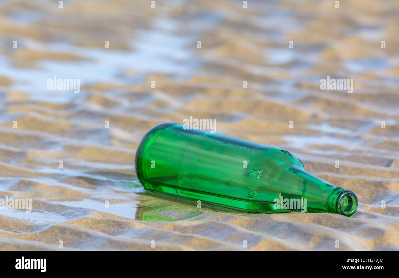 Verworfen, leere grüne Flasche links an einem Sandstrand. Stockfoto