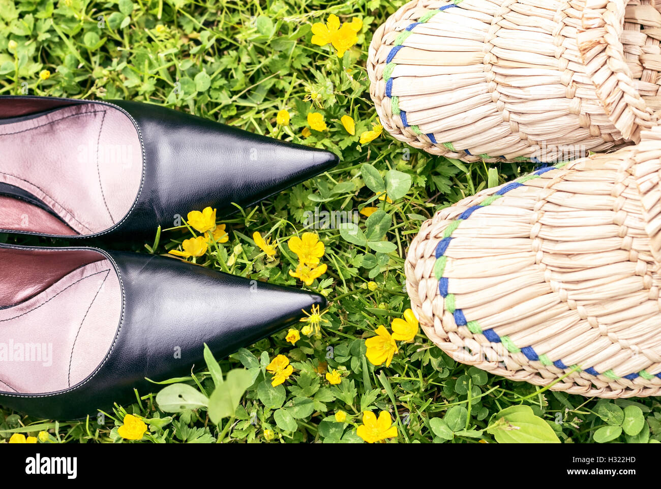 Schwarze Schuhe und Stroh geflochtenen Hausschuhe auf dem grünen Rasen wie Metapher über Stadt und Land Stockfoto