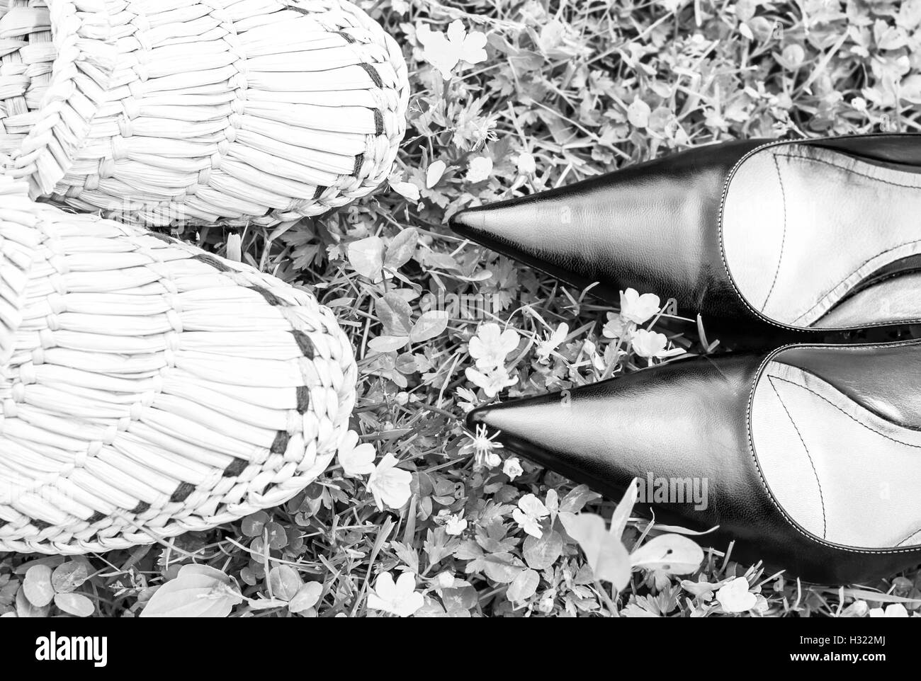 Schwarze Schuhe und Stroh geflochtenen Hausschuhe auf Rasen wie Metapher über Stadt und Land, in den Farben schwarz und weiß Stockfoto