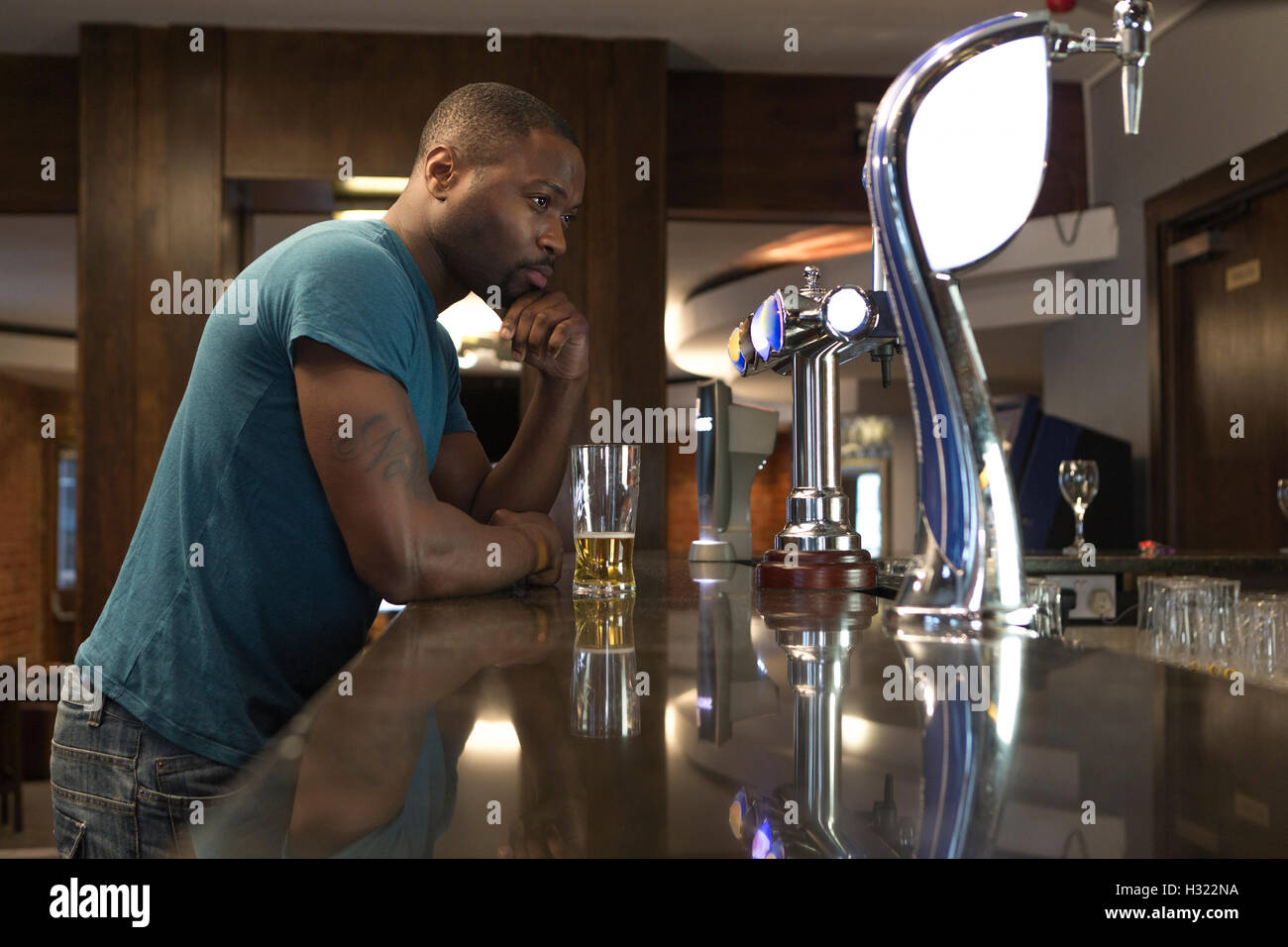 Junge Mann stand an der Bar aussehende tief in Gedanken versunken, mit einem Pint in der Hand. Stockfoto