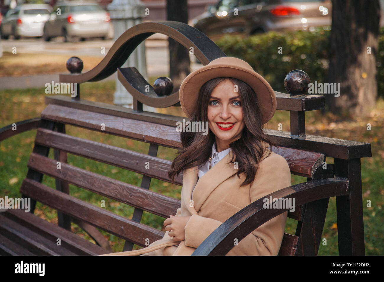 Porträt eines schönen Mädchens mit einem roten Lippenstift in einem Mantel auf einer Bank in einer Stadt-Gasse Stockfoto