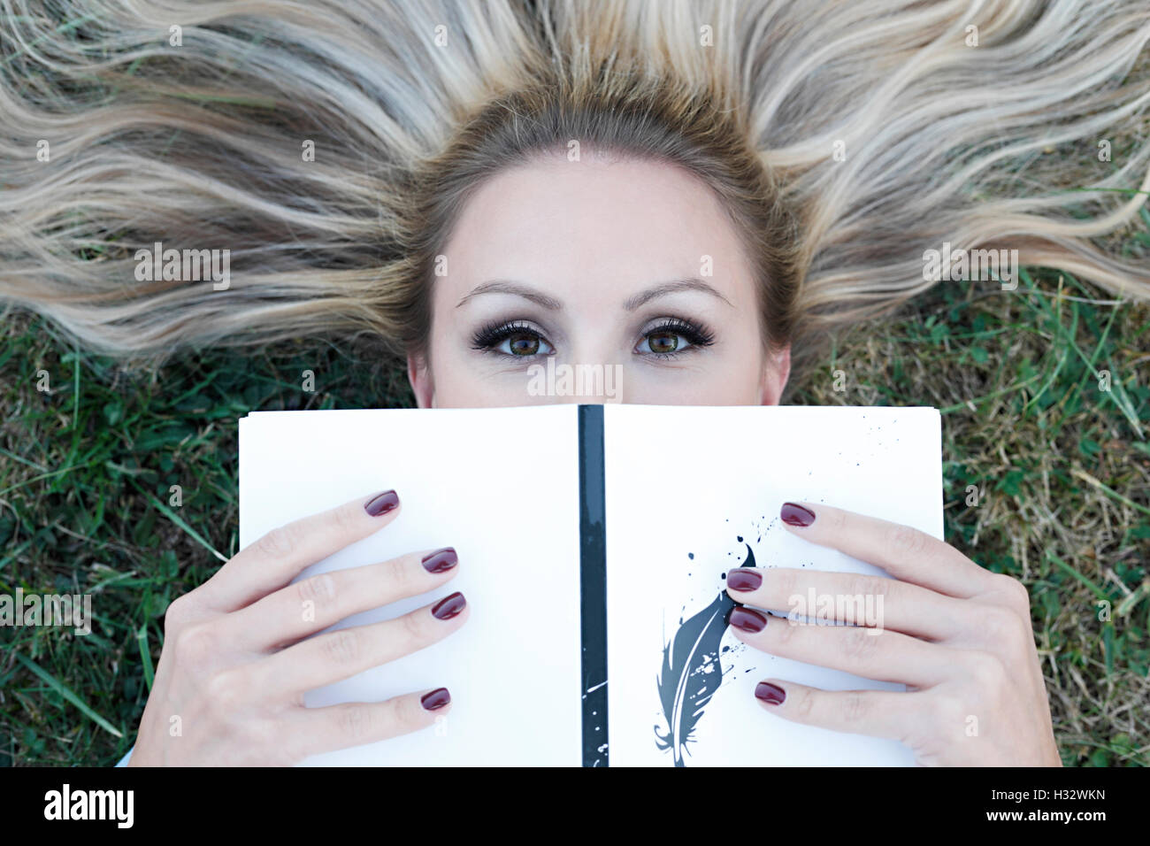 Schöne junge Blonde liegen auf dem Rasen mit einem Buch in ihren Händen Stockfoto