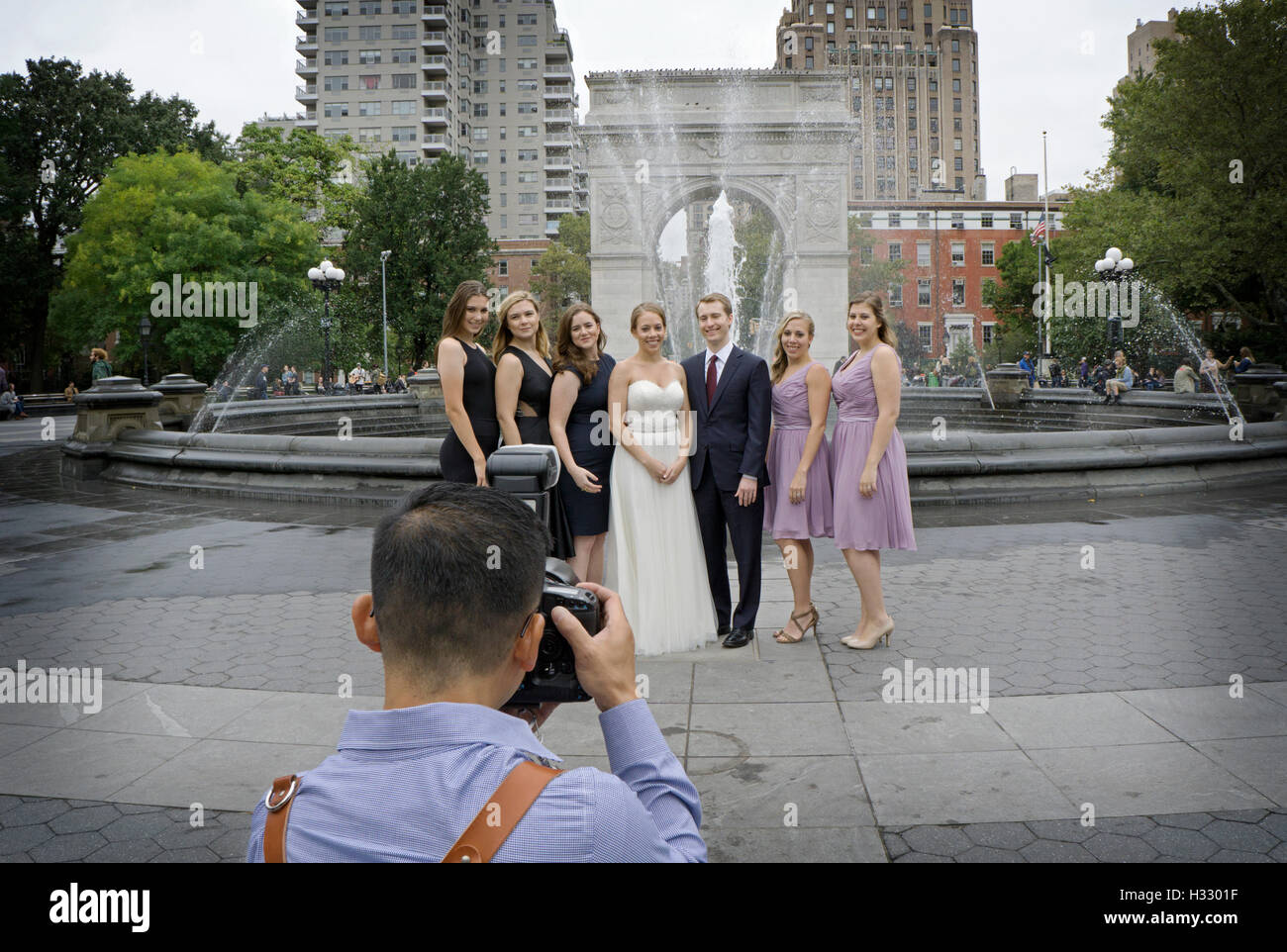 Eine asiatische Fotograf nimmt ein Gruppenfoto eines Hochzeitsfestes rund um den Brunnen im Washington Square Park in Greenwich Village. Stockfoto