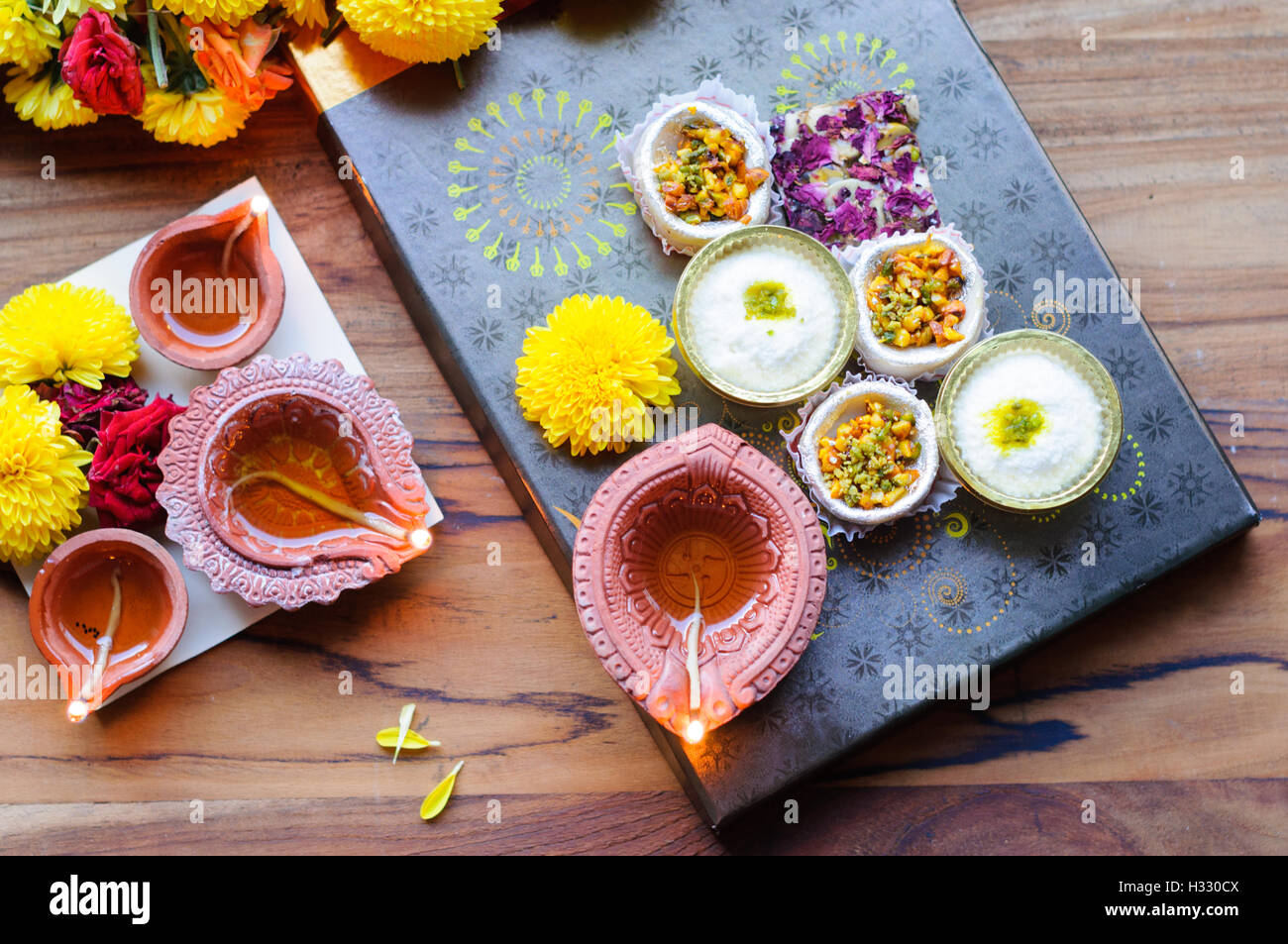 Diya Lampen angezündet während Diwali-fest mit Blumen und Süßigkeiten im Hintergrund Stockfoto