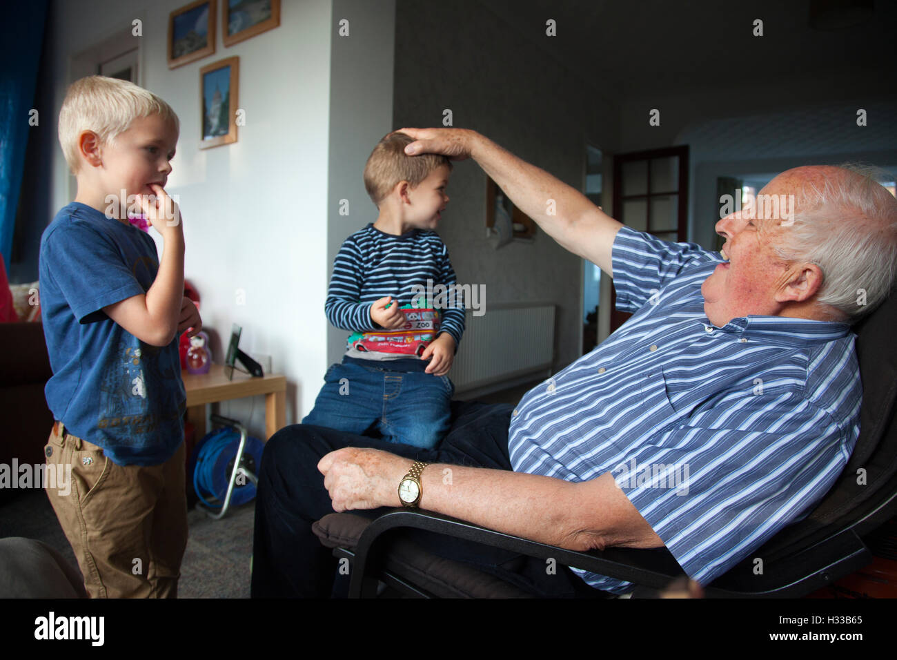 83 Jahre alte Großvater Interaktion mit seinen beiden jungen Enkel (im Alter von 3 und 6 Jahre alt) zu Hause in Hampshire, England, UK Stockfoto