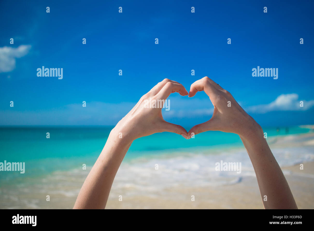 Schließen Sie oben des Herzens durch weibliche Hände Hintergrund das türkisblaue Meer Stockfoto
