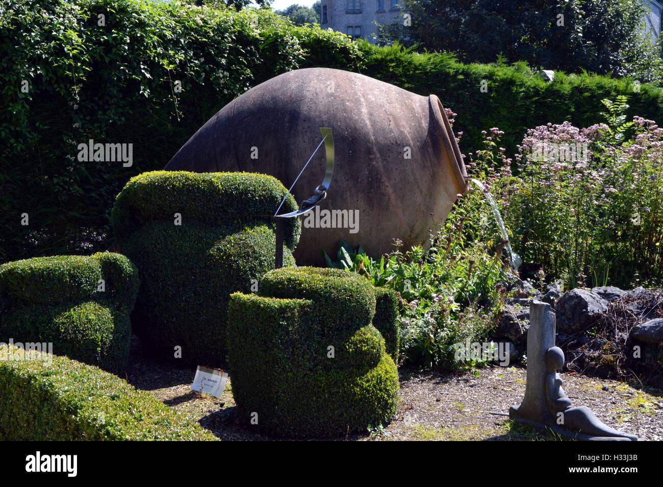 Riesige Amphore als Brunnen in der Mitte von Buchsbaum und mitten in einer Wiese. Stockfoto