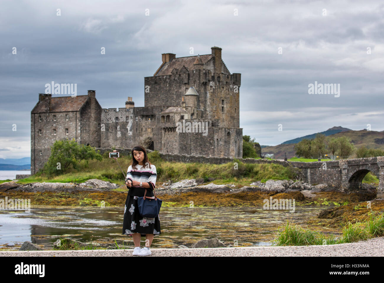 Asiatische Tourist, selfie mit Smartphone Kamera auf selfie Stick vor der schottischen Highlands Eilean Donan Castle, Schottland Stockfoto
