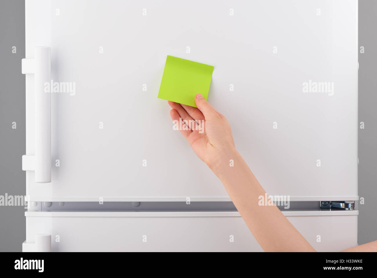 Weibliche Hand, die grüne klebrige Blankopapier Hinweis auf weißen Kühlschranktür Stockfoto