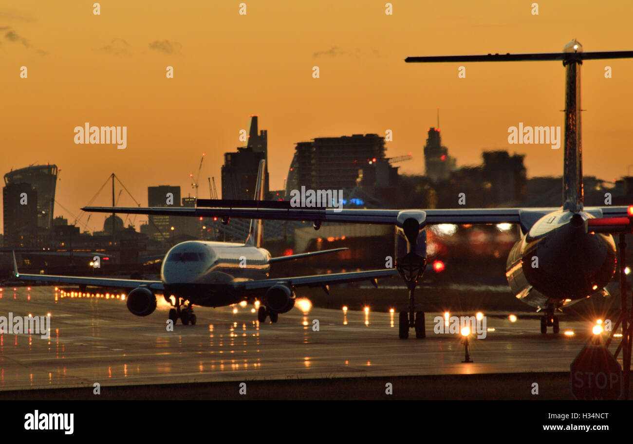 BA CityFlyer Rücken-Tracks während FlyBe Dash 8 wartet darauf, vom London City Airport ausziehen, wenn die Sonne untergeht Stockfoto