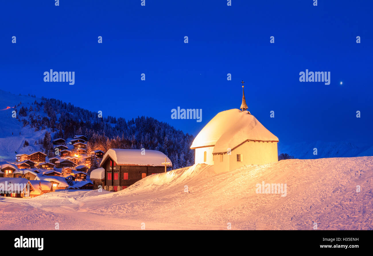 Blaue Dämmerung auf der alpinen Dorf und Kirche bedeckt mit Schnee, Bettmeralp, Bezirk Raron, Kanton Wallis, Schweiz Stockfoto