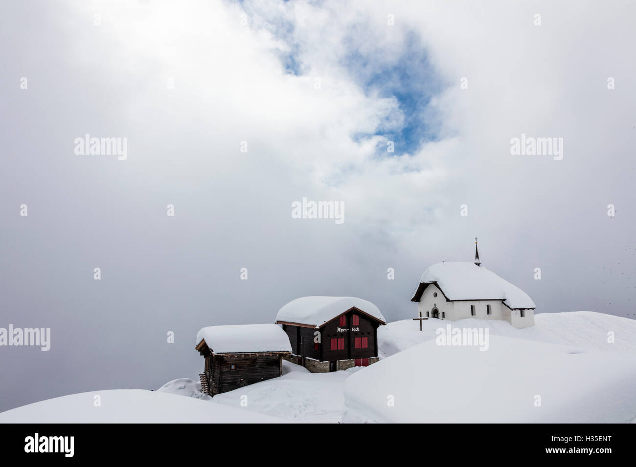 Verschneite Hütten und Kirche, umgeben von niedrigen Wolken, Bettmeralp, Bezirk Raron, Kanton Wallis, Schweiz Stockfoto