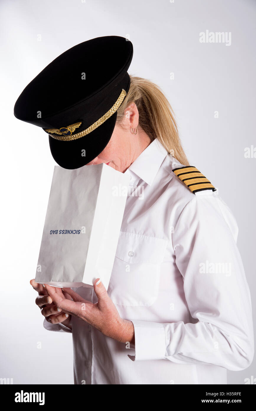 Frau mit einem Krankheit Tasche - A uniformierten weibliche pilot Gefühl Übel mit einer Papiertüte für Luft-Krankheit Stockfoto
