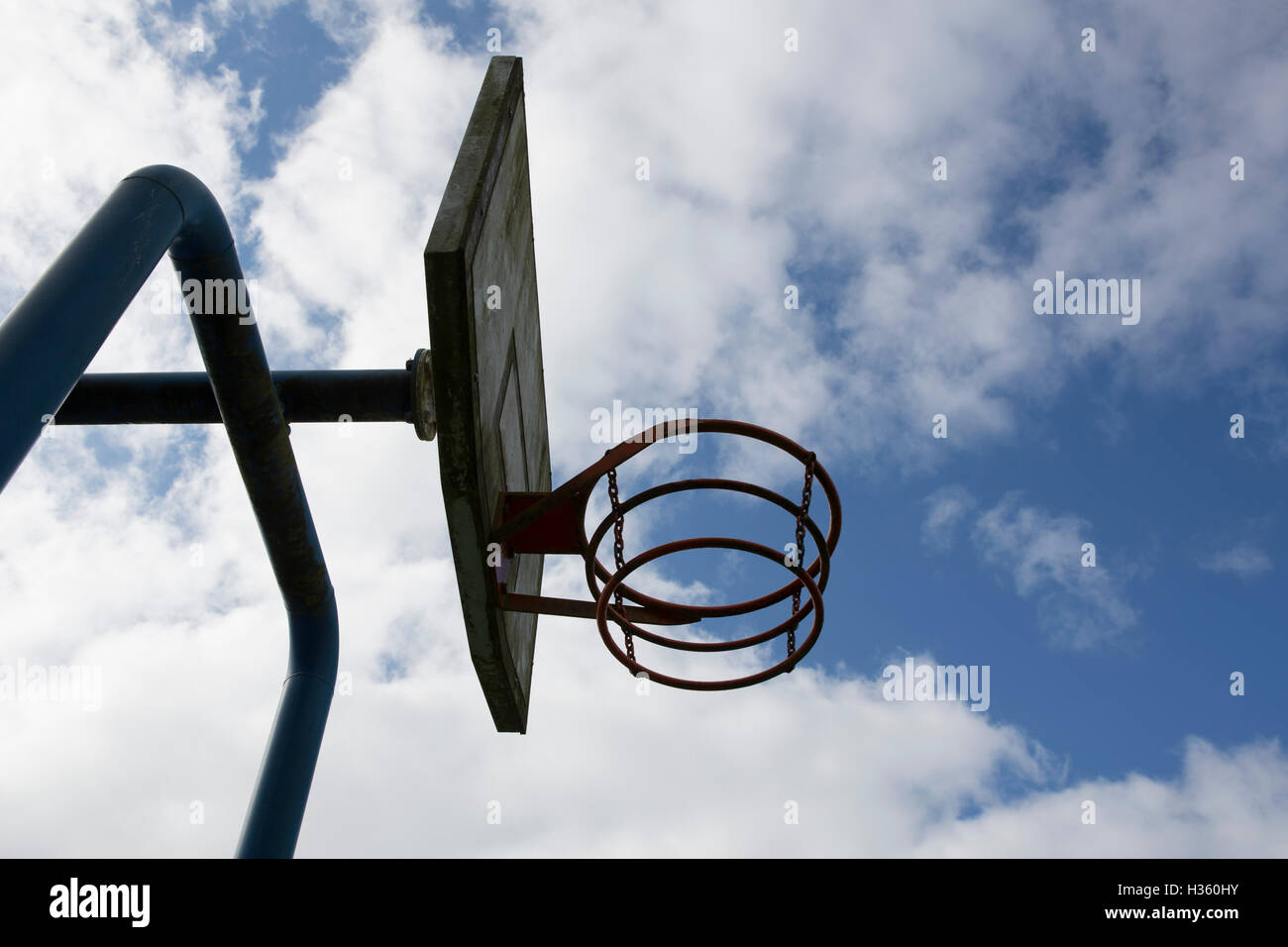 Alt und Metall Spielplatz Basketballkorb, inmitten einer Silhouette gegen einen hellen blauen und bewölkten Himmel. Stockfoto